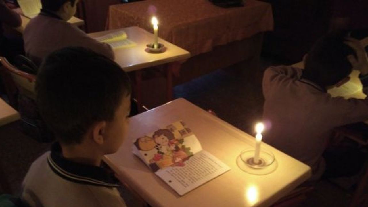 Minik öğrenciler mum ışığı eşliğinde kitap okuyor